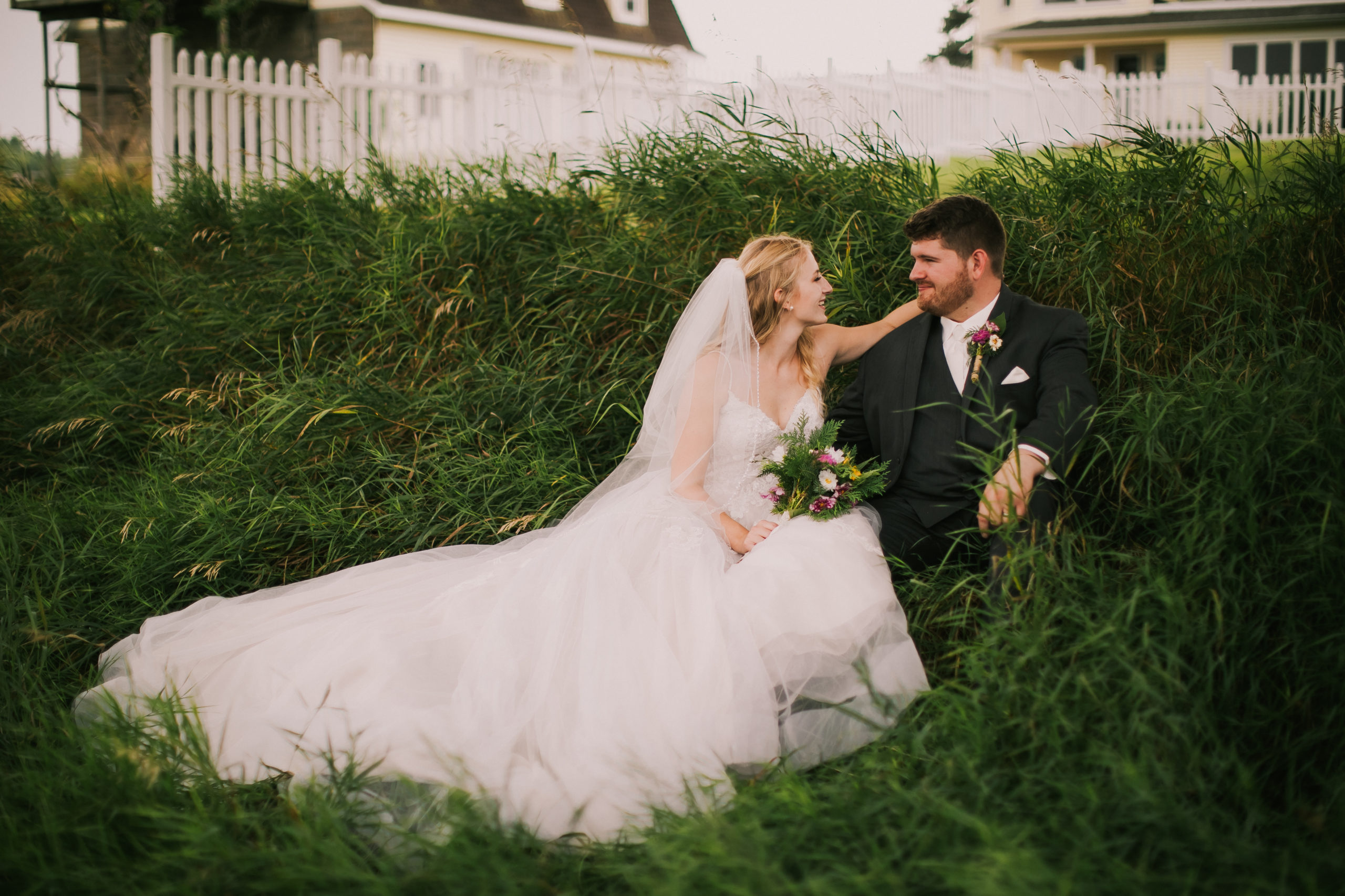 A bride and groom sit in the grass talking to each other